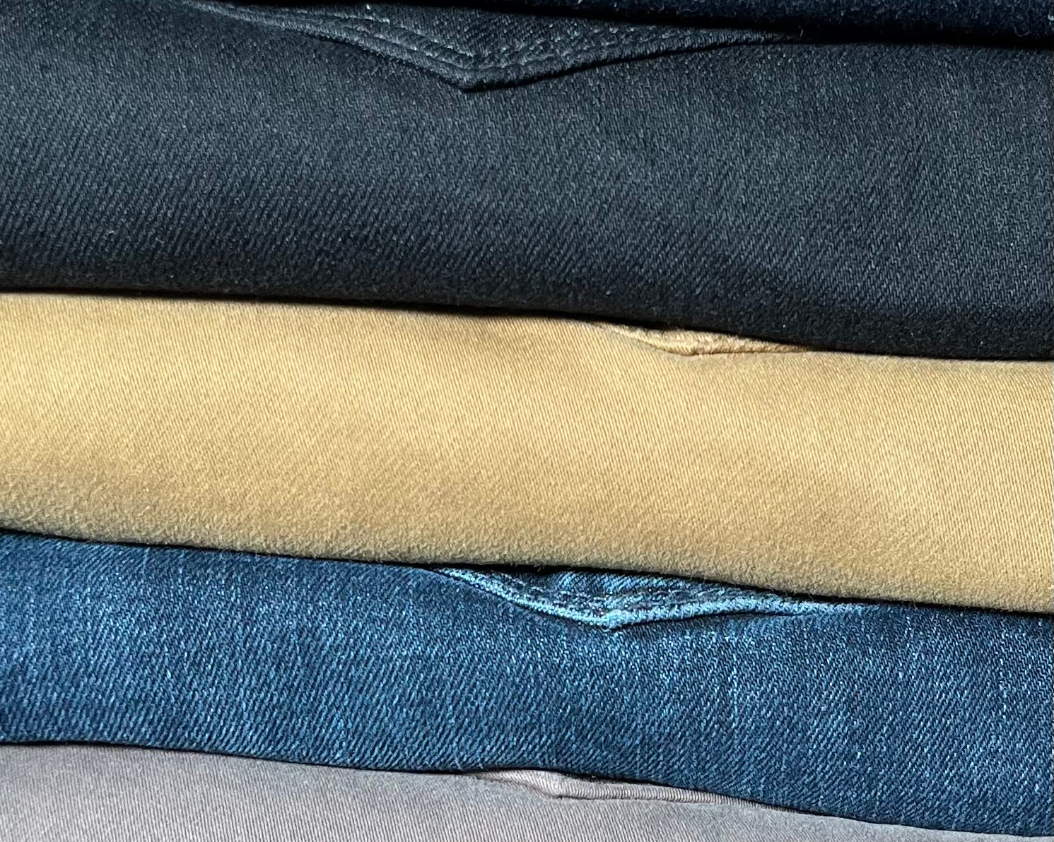 Stack of folded jeans in various colors on a wooden surface
