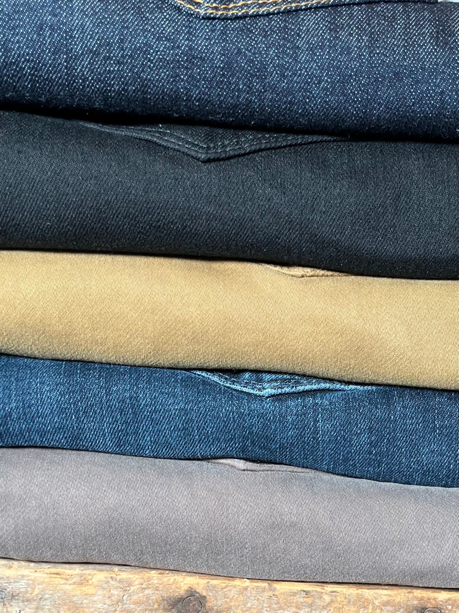 Stack of folded jeans in various colors on a wooden surface